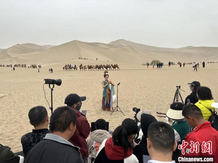 圖為2023年4月底，敦煌大漠“逐舞者”奧楠在鳴沙山月牙泉景區(qū)視頻直播，吸引游人圍觀?！●T志軍 攝