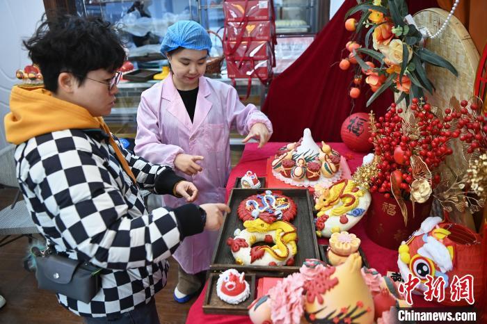 1月25日，隨著春節(jié)臨近，蘭州一花饃店“龍”元素花饃熱銷。圖為工作人員向顧客推薦“龍”元素花饃。九美旦增 攝</p><p>